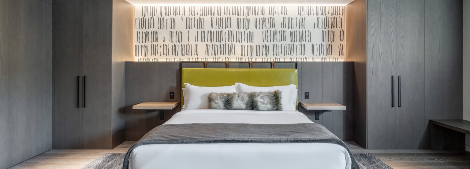 king bed in a grey modern bedroom with a white bedspread, and wallpaper