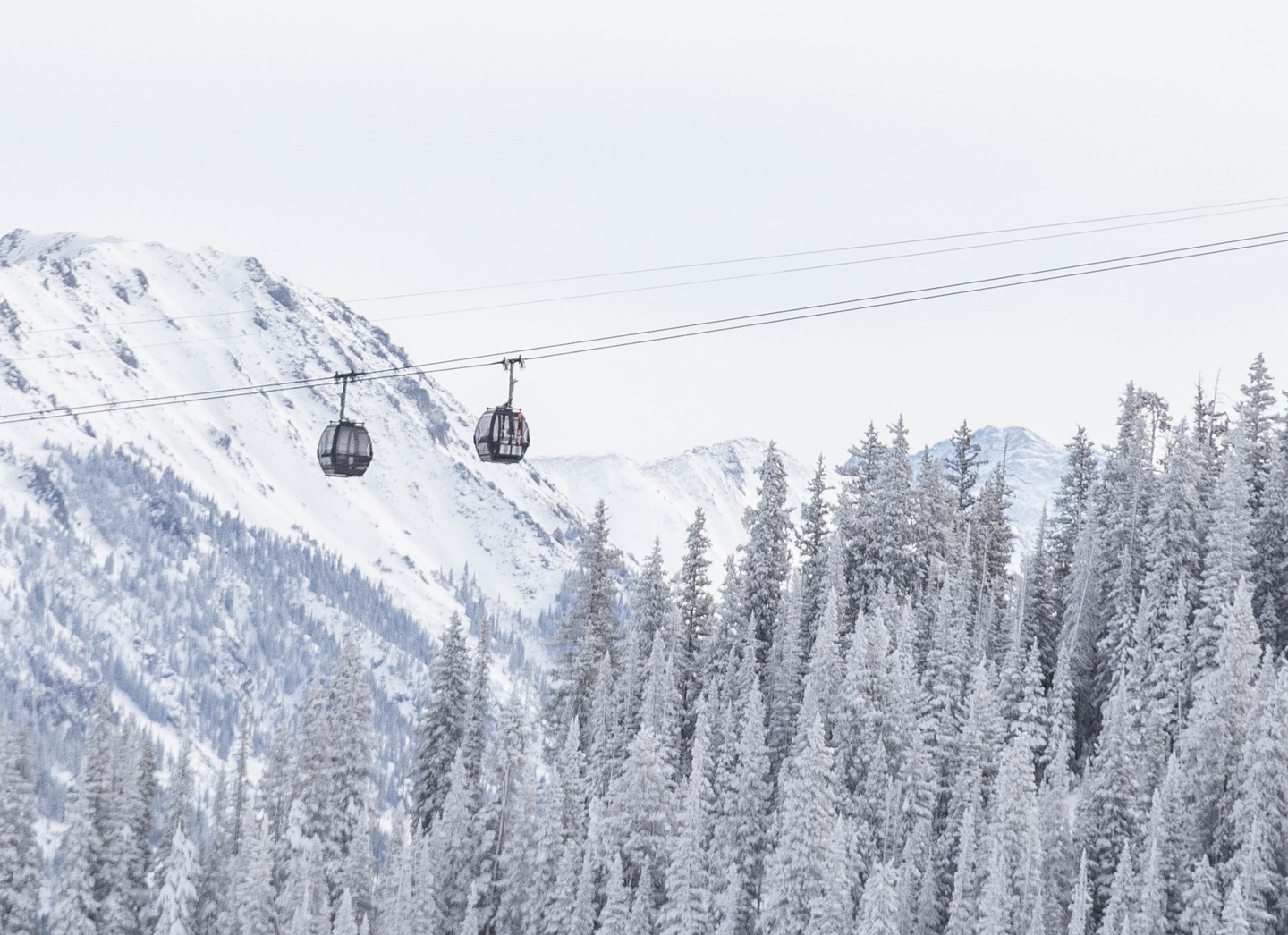 gondolas in aspen colorado in the winter with snowy mountains in the background and evergreen trees