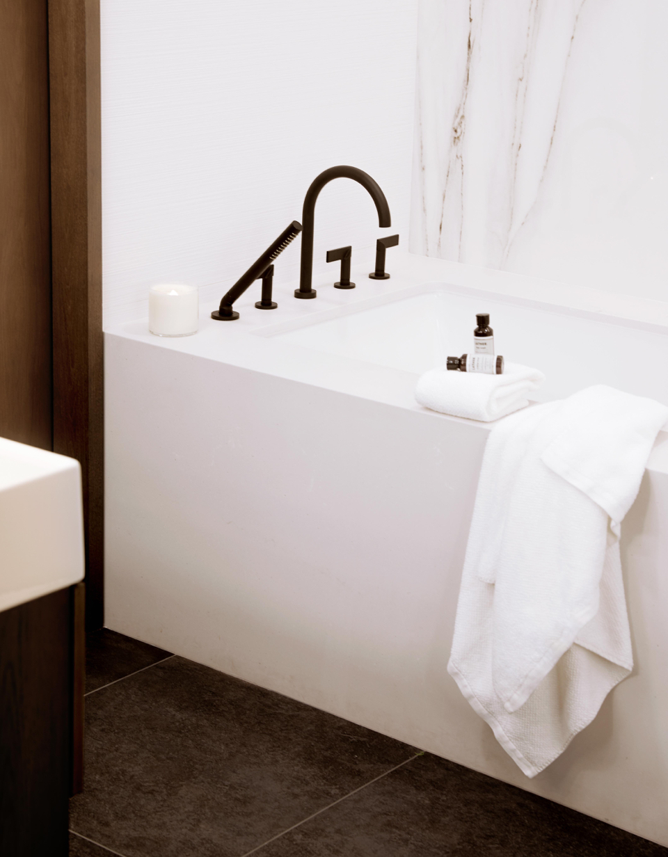 a modern, white stone bathtub with black faucet and handles and a fresh white towel and shampoo and conditioner