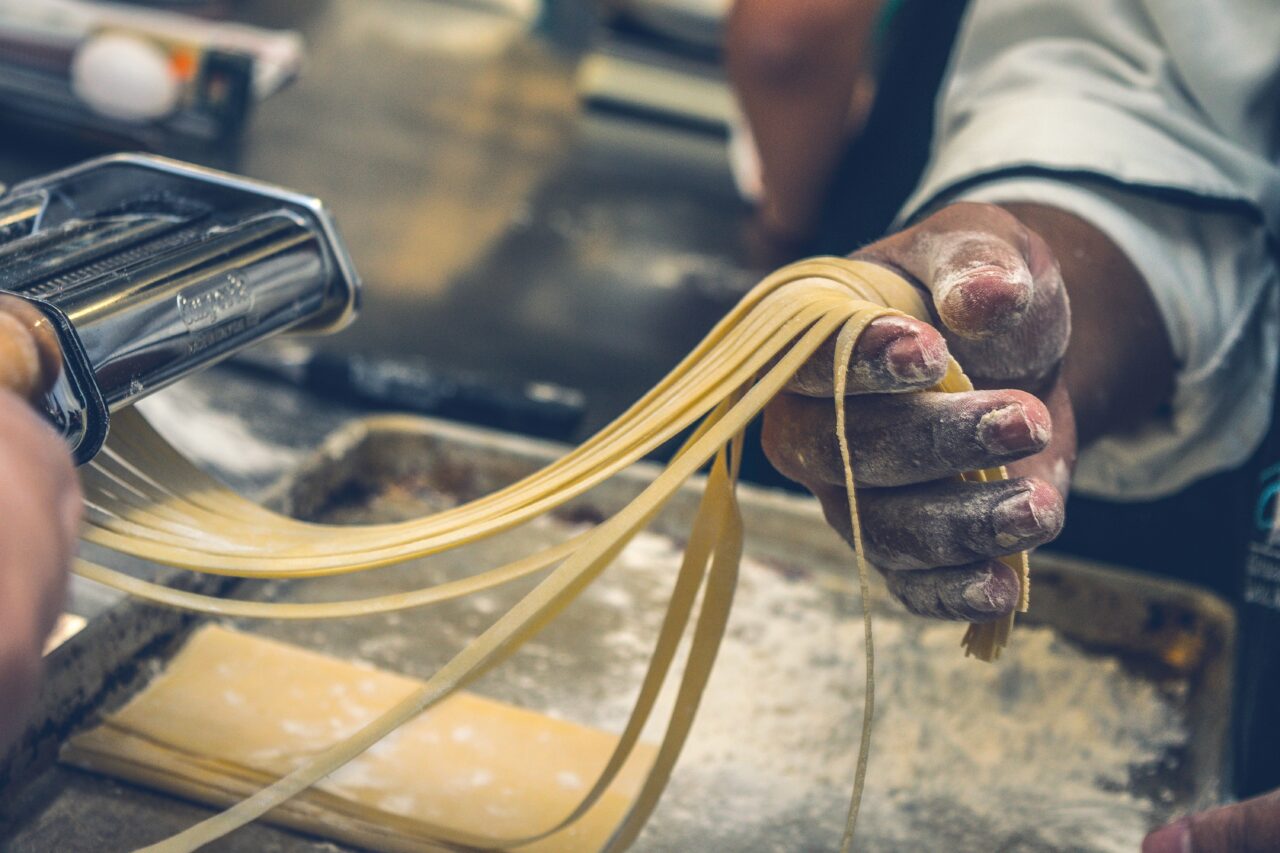 a chef holding homemade pasta from a pasta machine with flour on the page