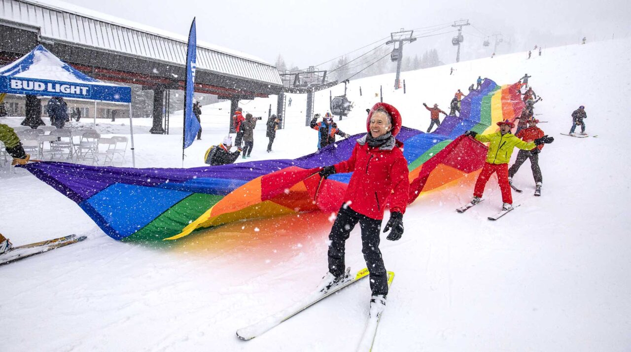 skiers holding a rainbow flag while on skis