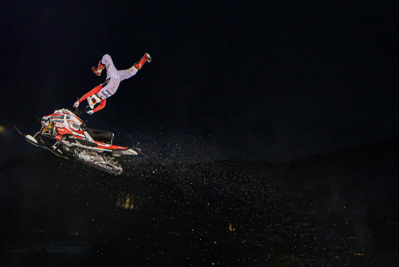 man hanging off a snowmobile at night in a dark sky