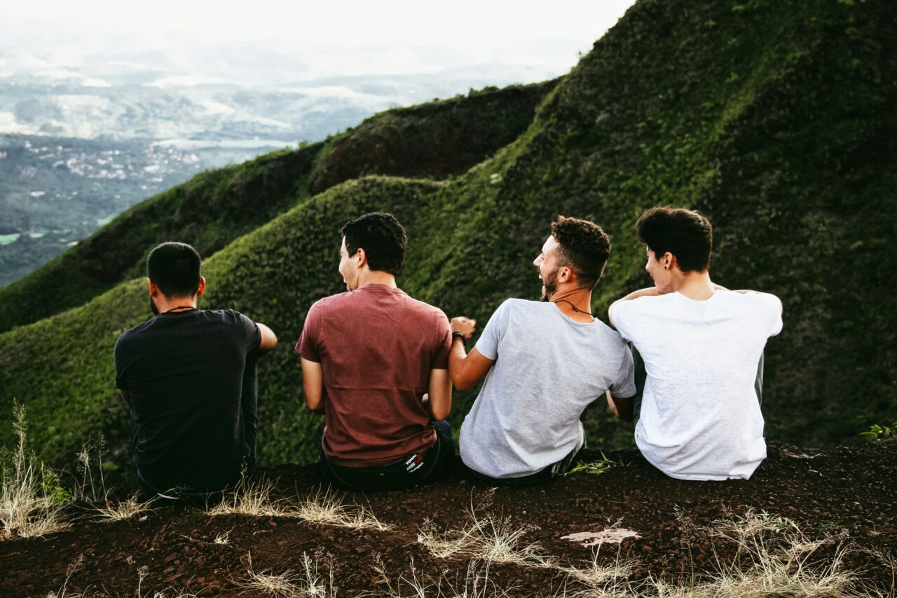 4 mens backs with a green mountain in the distance