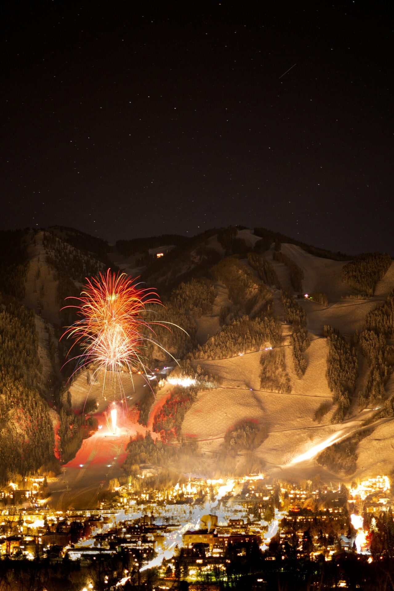 fireworks at night with a mountain and a town